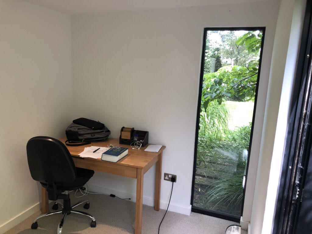 Minimal home office setup with a desk and chair next to a tall window overlooking a green garden