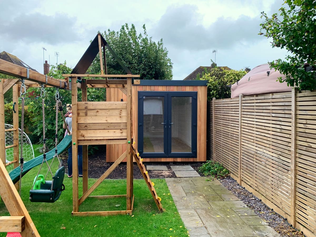 Cedar garden room at the end of a family garden beside a climbing frame