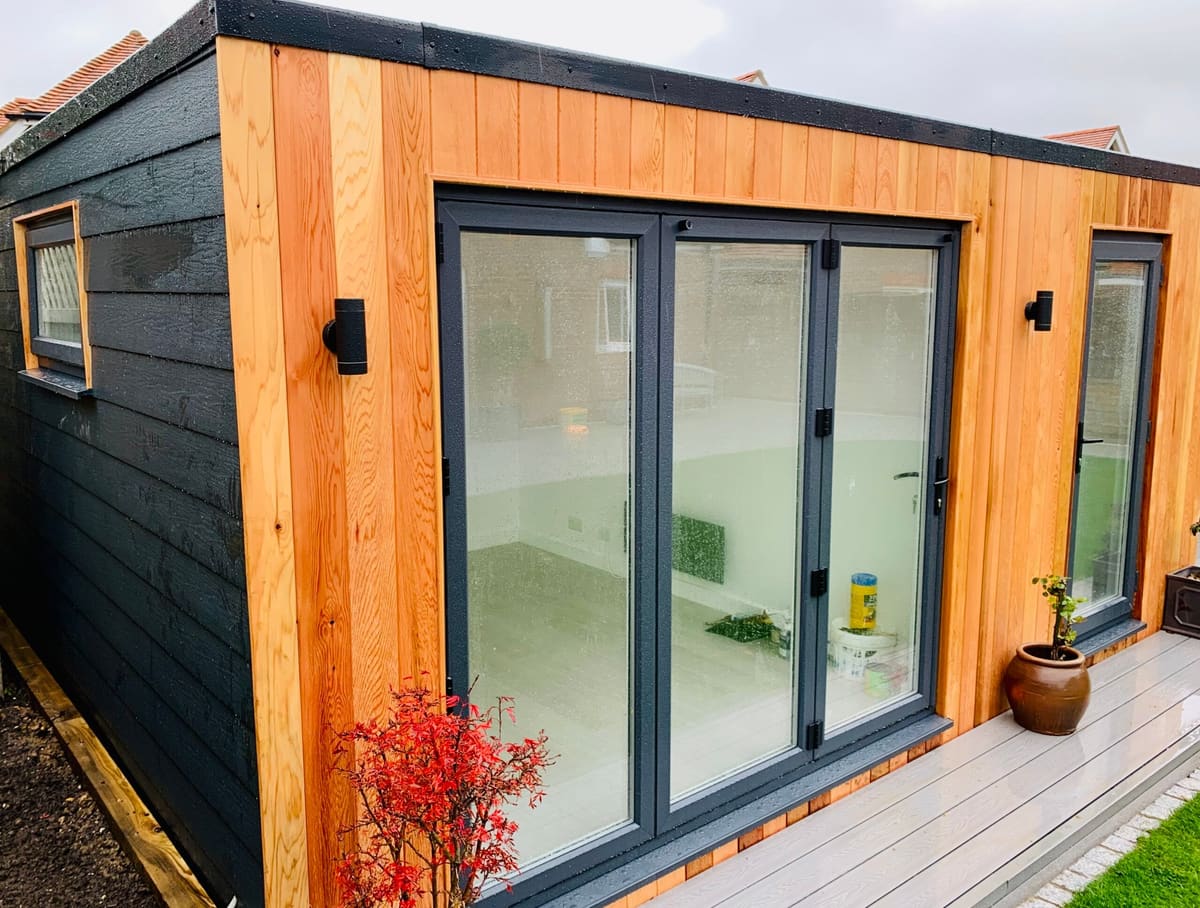 Timber and black-clad garden room with bi-fold doors and a grey deck