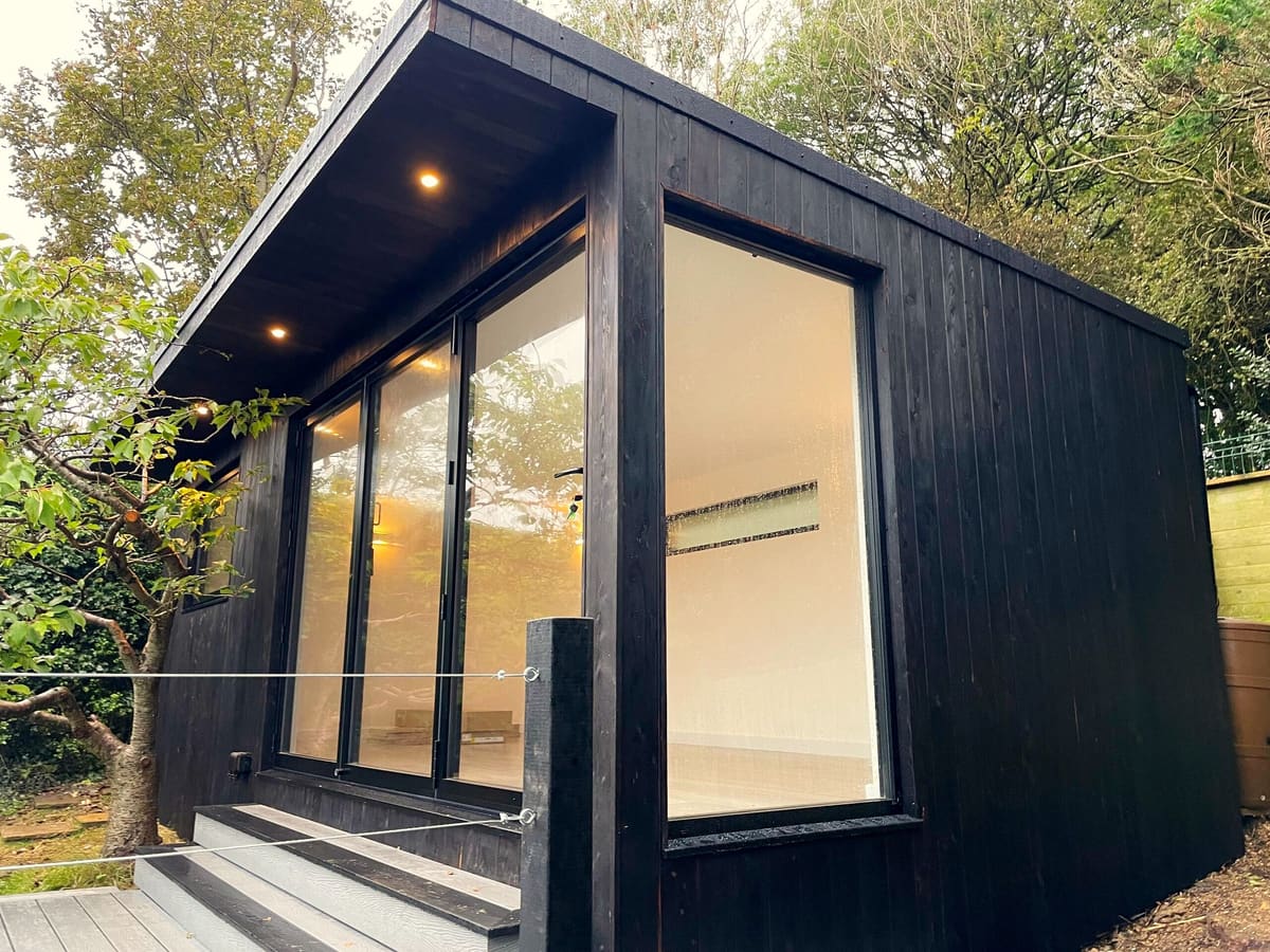 Dark timber garden office with lights on under the overhang, Brighton