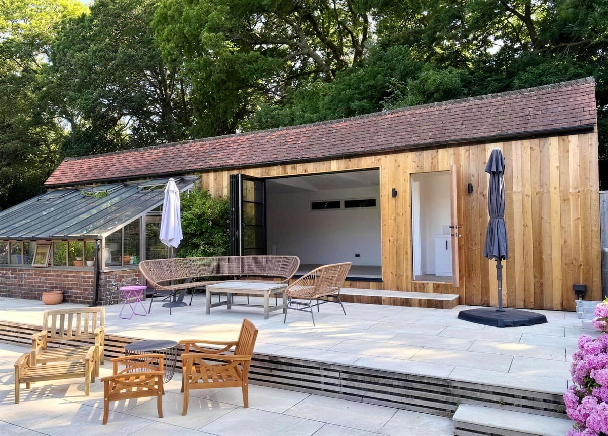 Cedar-clad barn conversion with patio seating beside a swimming pool in Haywards Heath