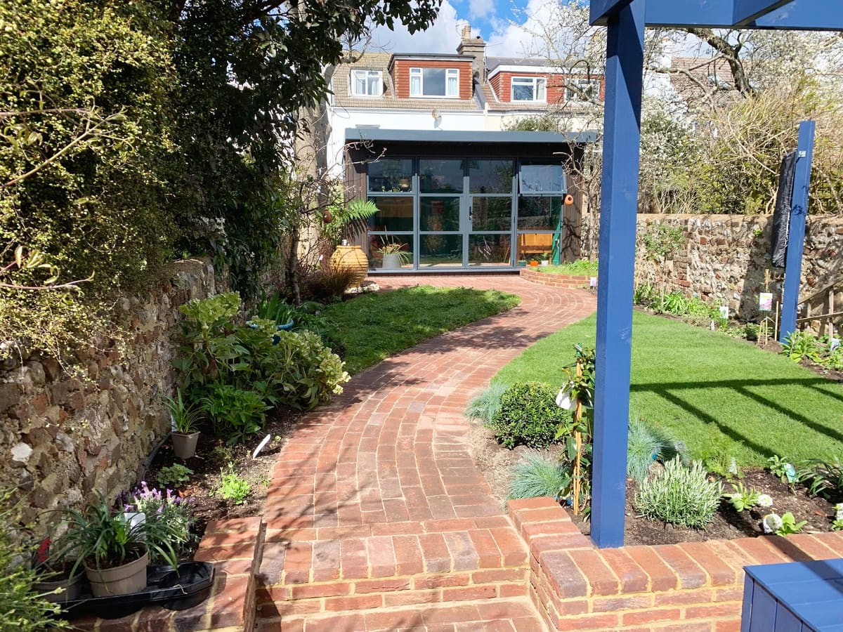 Brick path through a planted garden to a garden room